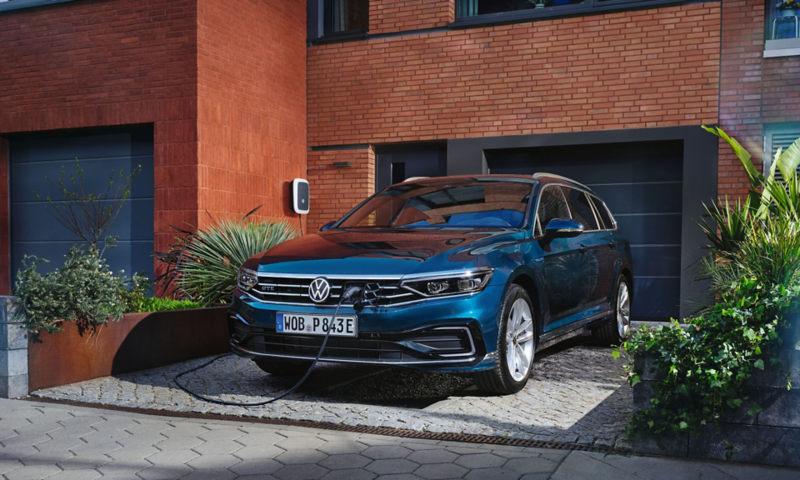 En blå VW Passat GTE Variant holder foran et hus, hvor den lades op med en ID. Charger-wallbox. 