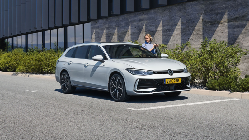 Une femme monte dans une VW Passat Variant blanche garée sur un parking devant un immeuble.