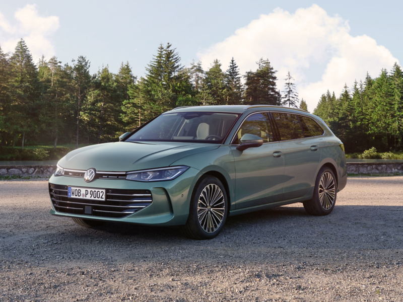 Zielononiebieski Volkswagen Passat stoi na żwirowym placu, w tle las iglasty.