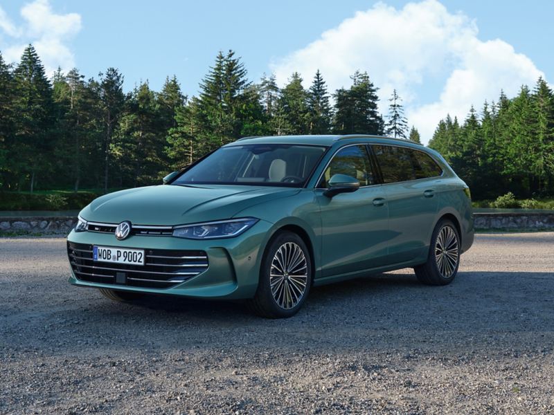 Bluish green VW Passat standing on a gravel surface, the area borders on a pine forest.