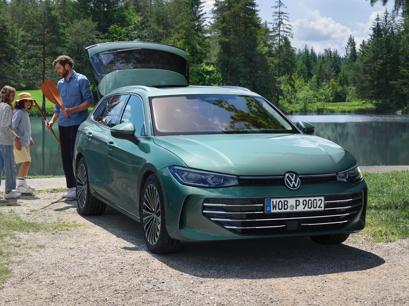 Une VW Passat garée près d'un lac avec le coffre ouvert. Un homme donne des affaires de plein-air à deux enfants.