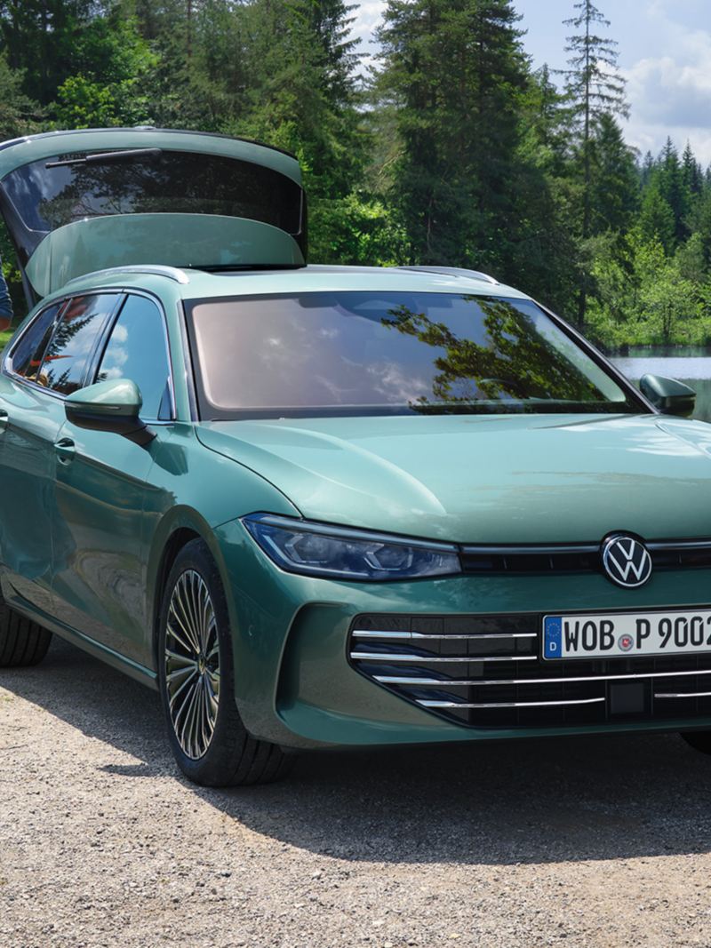 Bluish green VW Passat parked at a swimming lake with the luggage compartment open. A man hands out recreational toys to two children.