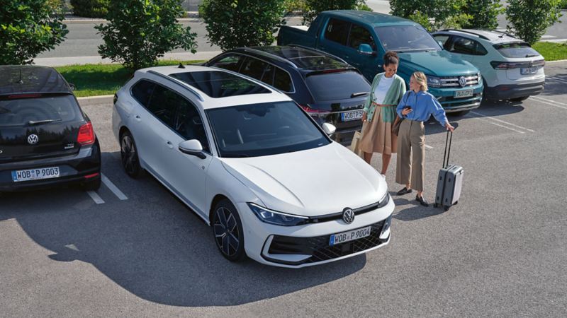 VW Passat steht auf einem Parkplatz, daneben zwei Personen mit Gepäck.