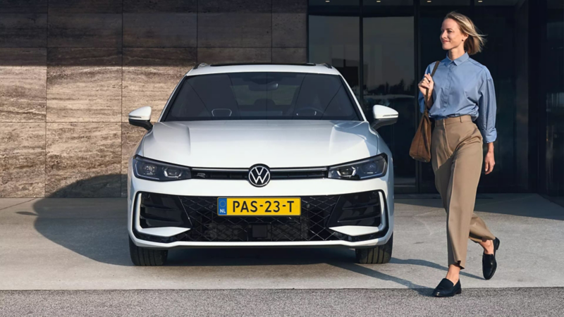 VW Passat eHybrid parked in front of a building, with a woman walking past it.