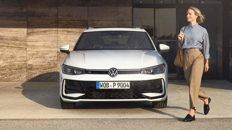 En VW Passat eHybrid holder parkeret med fronten udad ved en bygning, og en kvinde går foran bilen.
