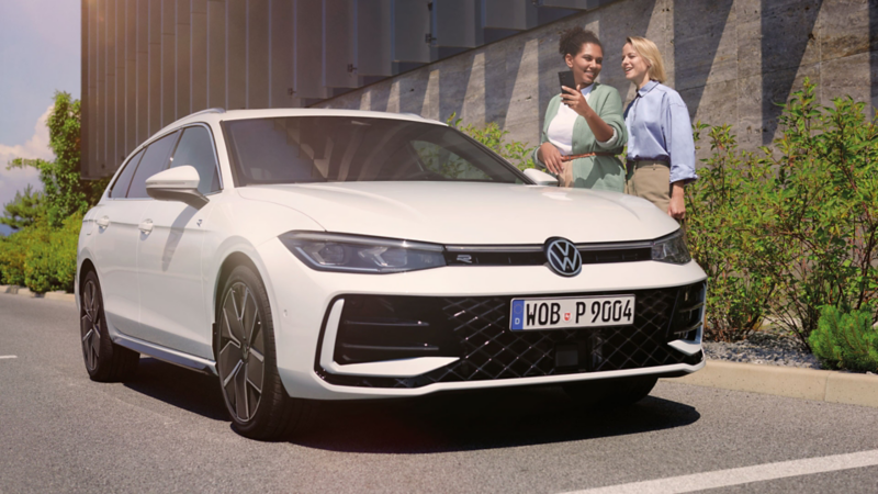 VW Passat parkt vor einem Bürogebäude, daneben zwei Frauen mit Smartphone.