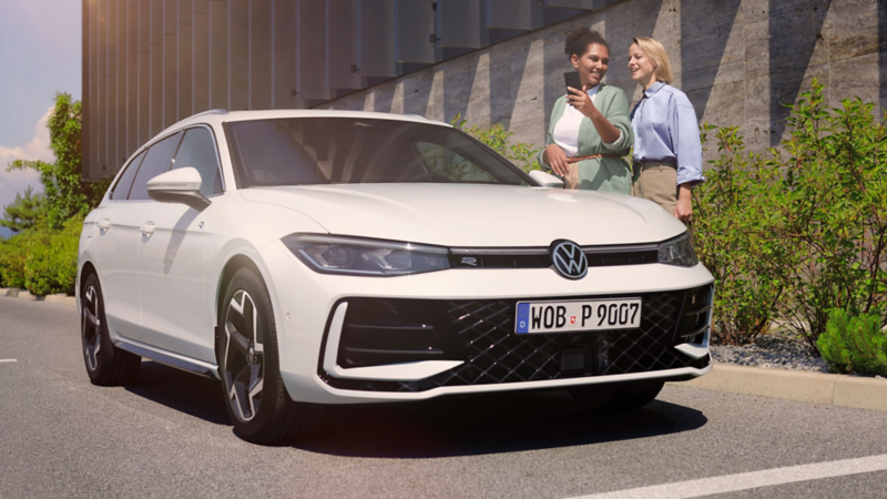 Deux femmes discutent derrière une Passat garée le long de la route, vue de 3/4 avant.