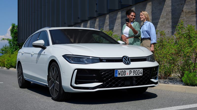 Deux femmes discutent derrière une Passat garée le long de la route, vue de 3/4 avant.