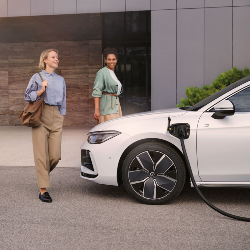 Passat GTE står på laddning utanför en byggnad, två kvinnor går mot bilen