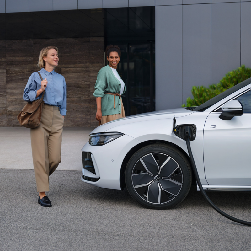 Passat GTE står på laddning utanför en byggnad, två kvinnor går mot bilen