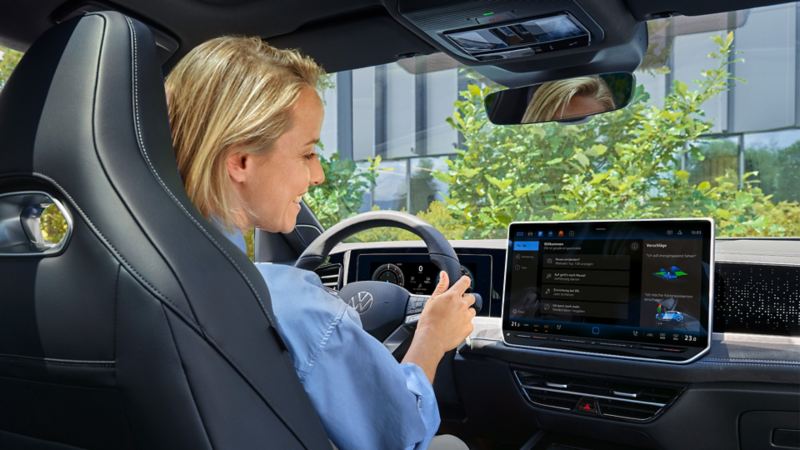 Sieviete sēž Volkswagen automašīnā un izmanto tiešsaistes balss asistentu