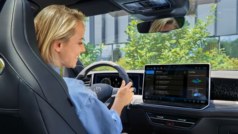 Junge Frau blickt auf das Display eines Volkswagen und kommuniziert mit dem Sprachassistent.