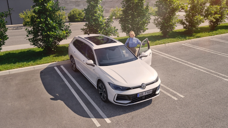 Eine Frau steigt auf einem begrünten Parkplatz in einen VW Passat ein.