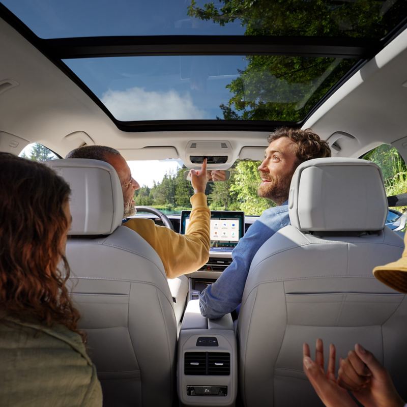 Wnętrze VW Passata, w którym siedzi dwoje dzieci i dwóch mężczyzn. Widok z tylnej kanapy na przednie siedzenia i opcjonalny dach panoramiczny.