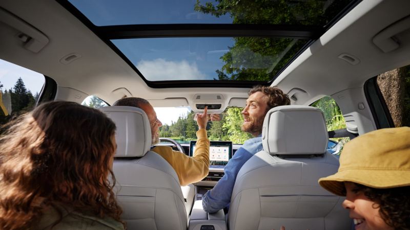 Interior of the VW Passat with two children and two men on board: view from the rear bench seat to the front seats and the optional tilting and sliding panoramic sunroof.