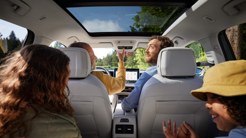 Sisänäkymä Passatiin, jossa on 4 henkilöä, ja näkymä kohti infotainment-järjestelmää ja panoraamalasikattoa/-kattoluukkua