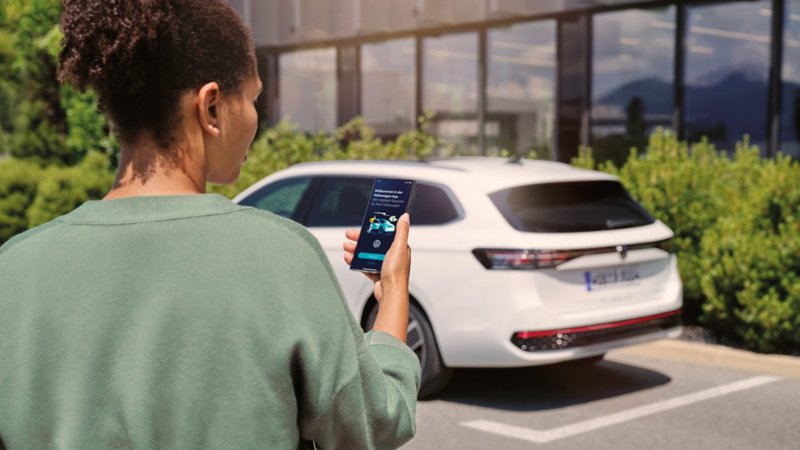 VW Passat blanche garée devant un immeuble. Vue arrière d'une femme regardant son smartphone.