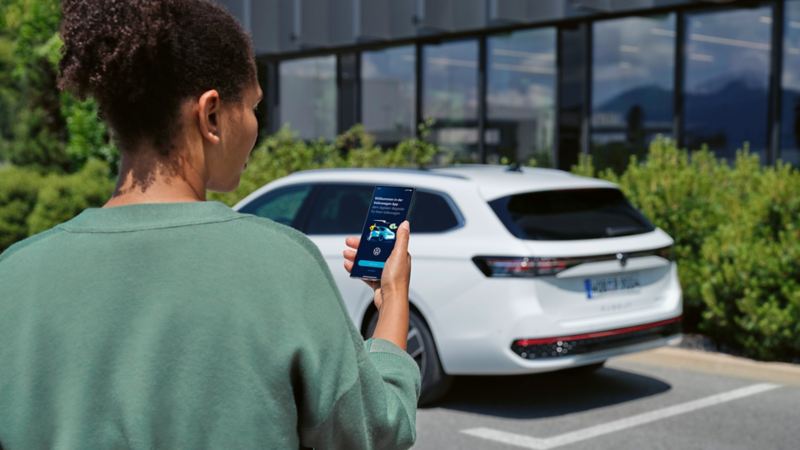 VW Passat blanche garée devant un immeuble. Vue arrière d'une femme regardant son smartphone.
