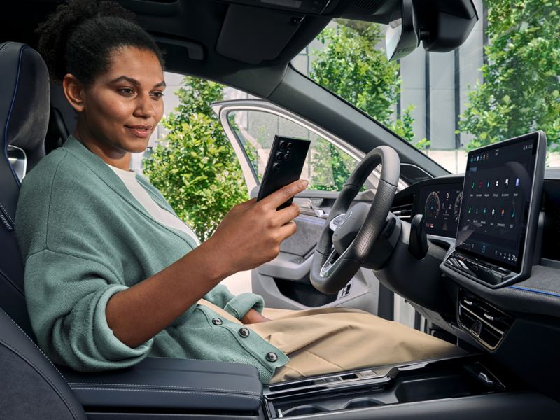 Cilvēks sēž Volkswagen automašīnā un skatās mobilajā tālrunī