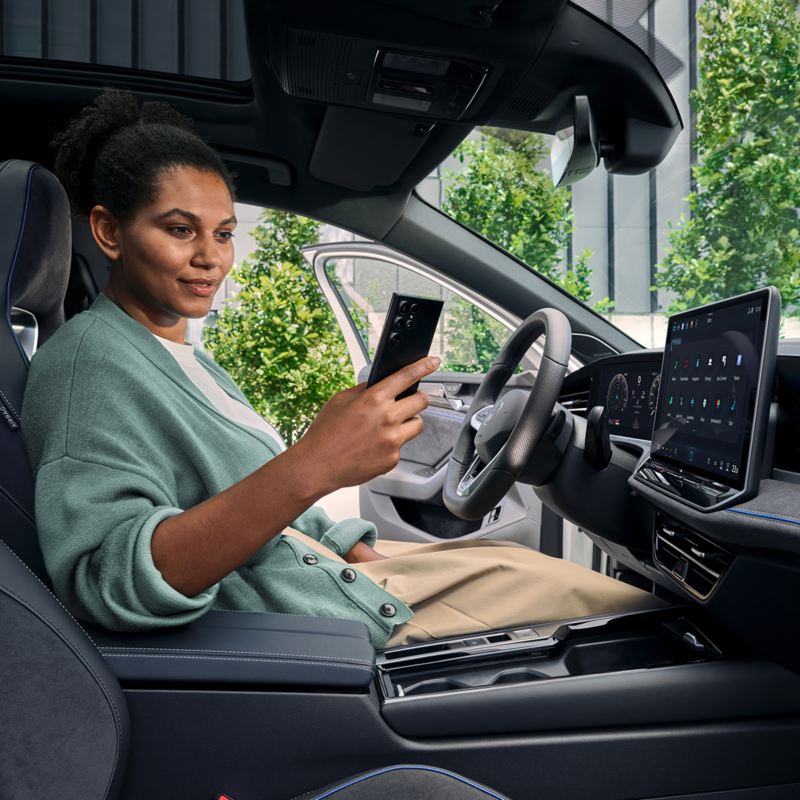 Asmuo sėdi „Volkswagen“ automobilyje ir žiūri į mobilųjį telefoną