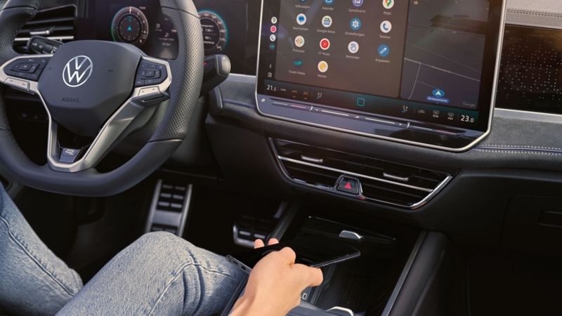 Vue détaillée du cockpit de la Volkswagen Passat. Quelqu’un est assis sur le siège conducteur et tient un smartphone à la main.