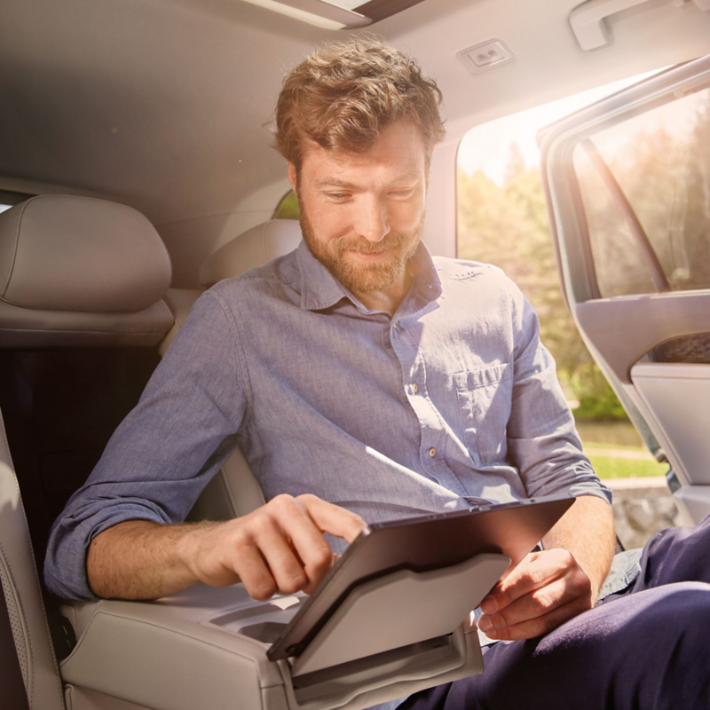 Ein Mann auf der Rückbank des VW Passat hat sein Tablet auf der Halterung der Mittelarmlehne platziert. 