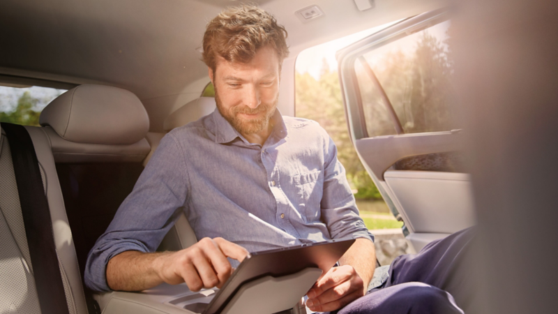 Ein Mann auf der Rückbank des VW Passat hat sein Tablet auf der Halterung der Mittelarmlehne platziert. 
