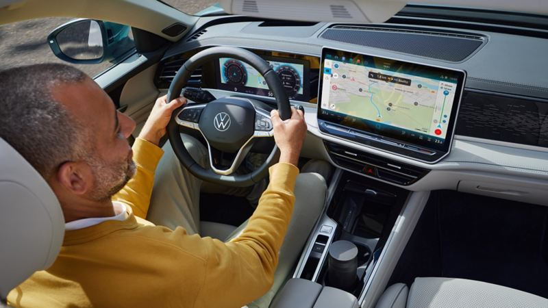 Vue en plongée à travers le toit ouvrant coulissant (en option) de la VW Passat, où un homme est assis avec les deux mains sur le volant.