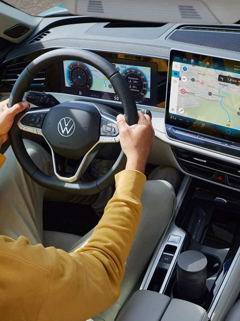 Bovenaanzicht door het open optionele schuifdak van de VW Passat, waar een man met beide handen aan het stuur zit.