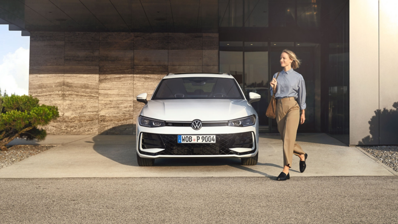 Frau geht vor einem parkenden Passat entlang, im Hintergrund ein modernes Gebäude.