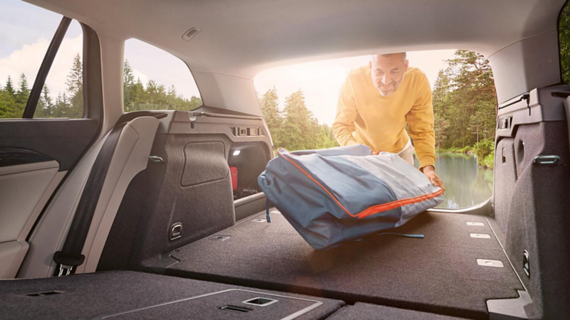 Un homme vêtu d'un pull jaune range un bagage dans le coffre dont la banquette arrière est rabattue.