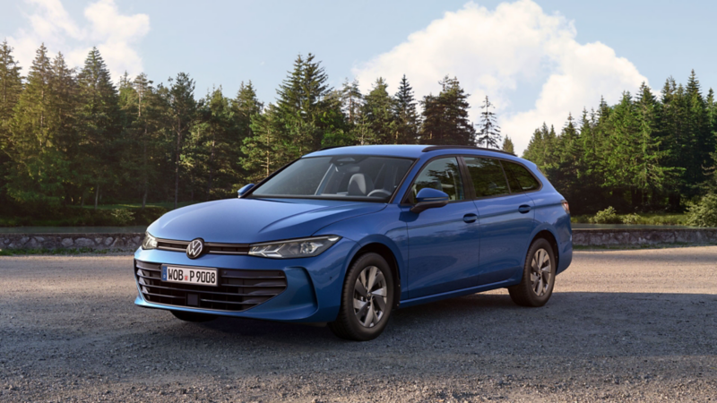 VW Passat in blau steht auf einer Kiesfläche, im Hintergrund ein Tannenwald.