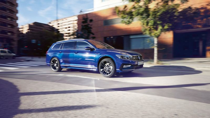 Blauer VW Passat Variant fährt dynamisch durch eine Stadt. Blick auf Seite, Räder und Leuchten.