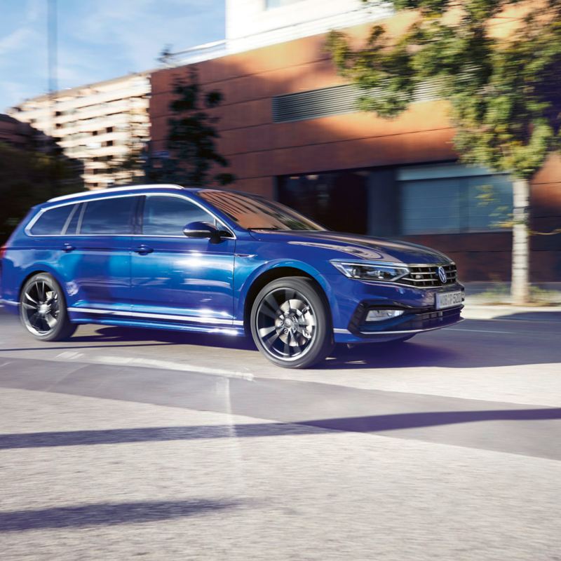 Blauer VW Passat Variant fährt dynamisch durch eine Stadt. Blick auf Seite, Räder und Leuchten.