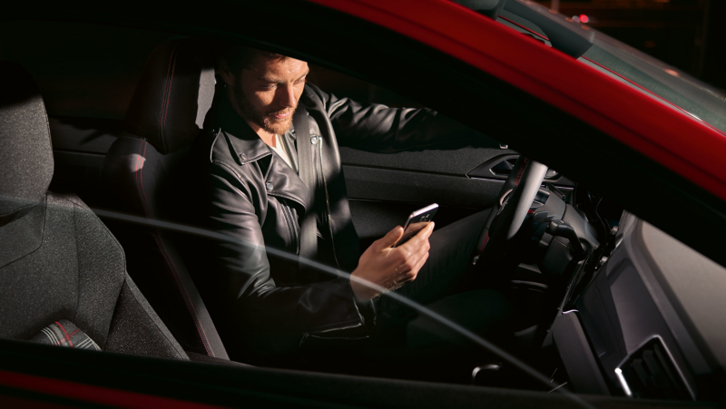 Mężczyzna siedzi za kierownicą Polo GTI i sprawdza coś w telefonie. 