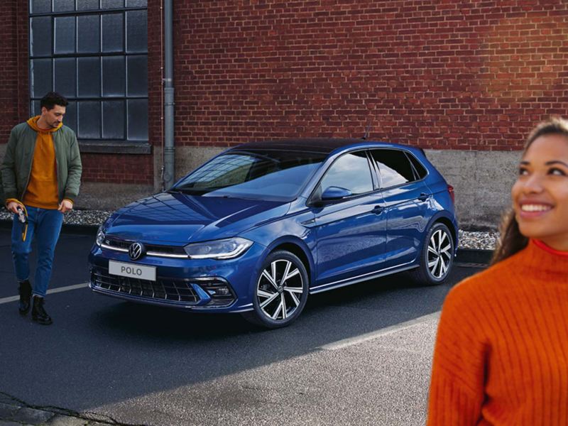 Une VW Polo bleue visible devant une rampe, un homme passe devant l’arrière doté des feux arrière à LED en option.