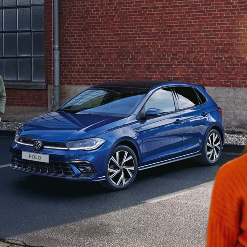 Une VW Polo bleue visible devant une rampe, un homme passe devant l’arrière doté des feux arrière à LED en option.