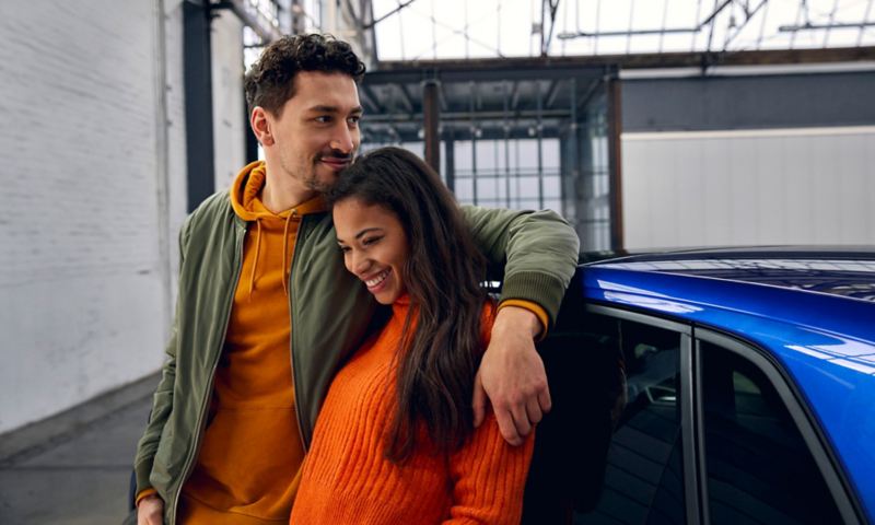 A couple leans against a new blue Polo. 