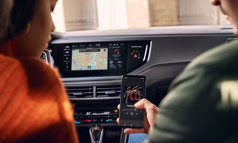 Dwie osoby siedzą z przodu w VW Polo, prawa trzyma smartfona, który łączy się bezprzewodowo z systemem Infotainment.