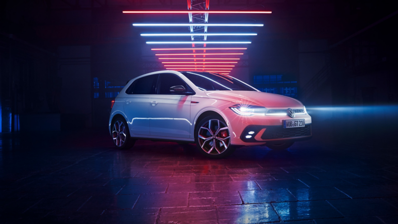 Ein weißer VW Polo GTI mit aktiven Scheinwerfern in einer dunklen Lagerhalle.