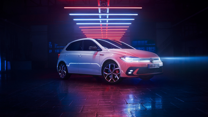 View from the rear of a white Polo GTI under light elements in a dark hall with LED tail light clusters switched on.