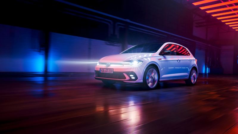 A white VW Polo GTI drives in a hall with LED matrix headlights switched on and light strip in the front