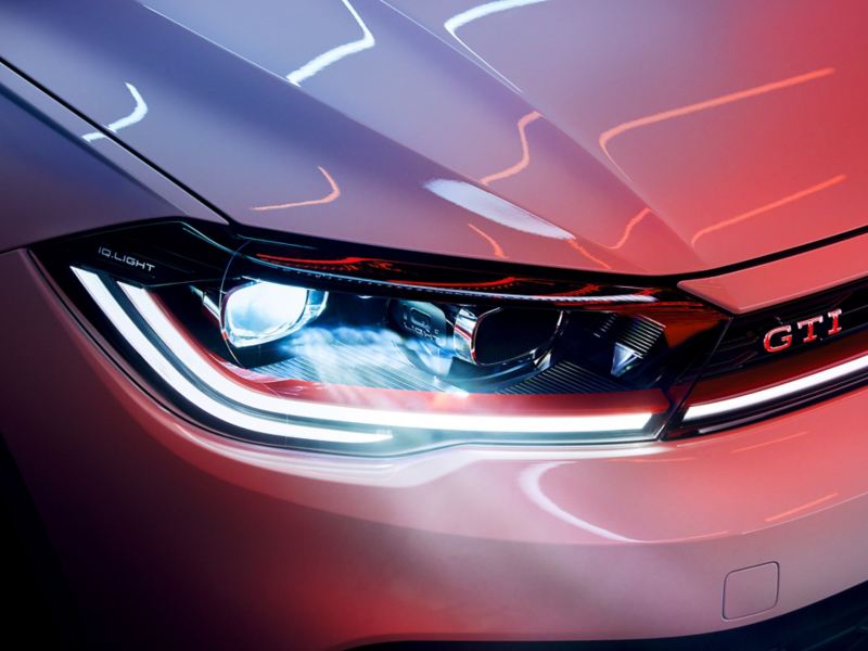 Close-up of the LED matrix headlights at the front of a white VW Polo GTI, red decorative strips and GTI badge discernible.