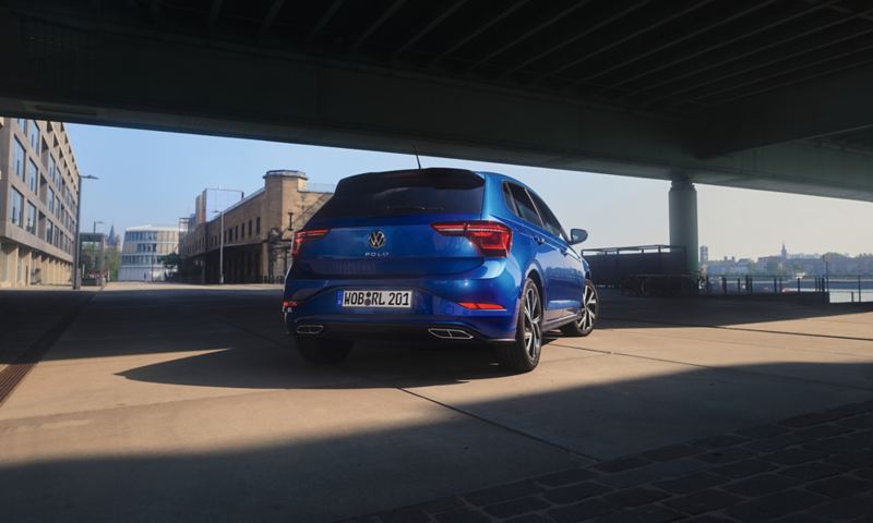 Une VW Polo bleue en vue arrière aux vitres arrière teintées se trouve sous un pont.