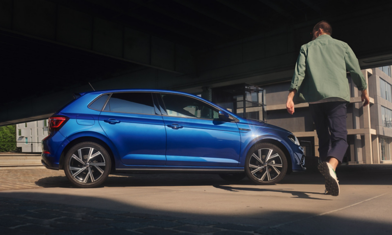 Polo bleue stationnée, vue de profil. Un homme de dos avance vers la voiture.