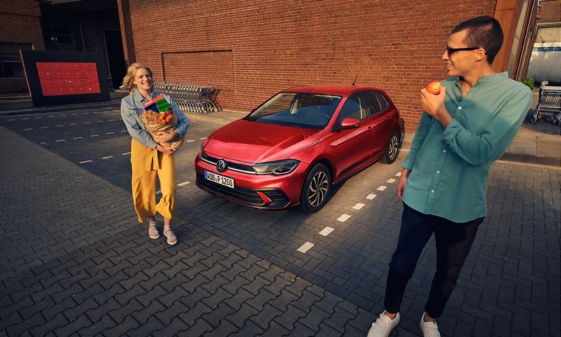 VW Polo rouge garée, une femme avec des courses