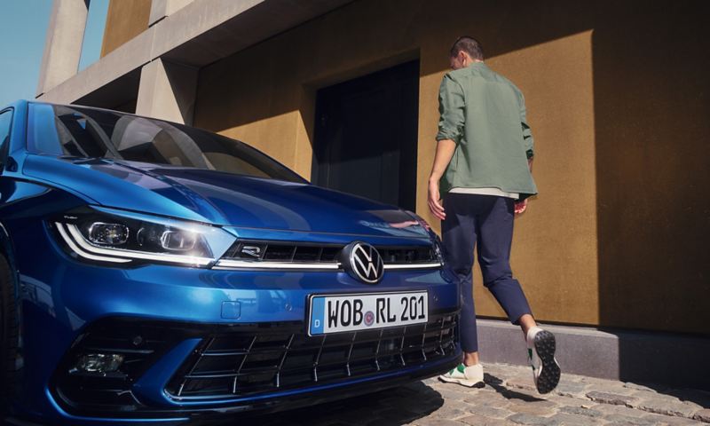 Avant d'une Volkswagen Polo bleue stationnée dans une rue avec un homme qui marche à côté du véhicule.