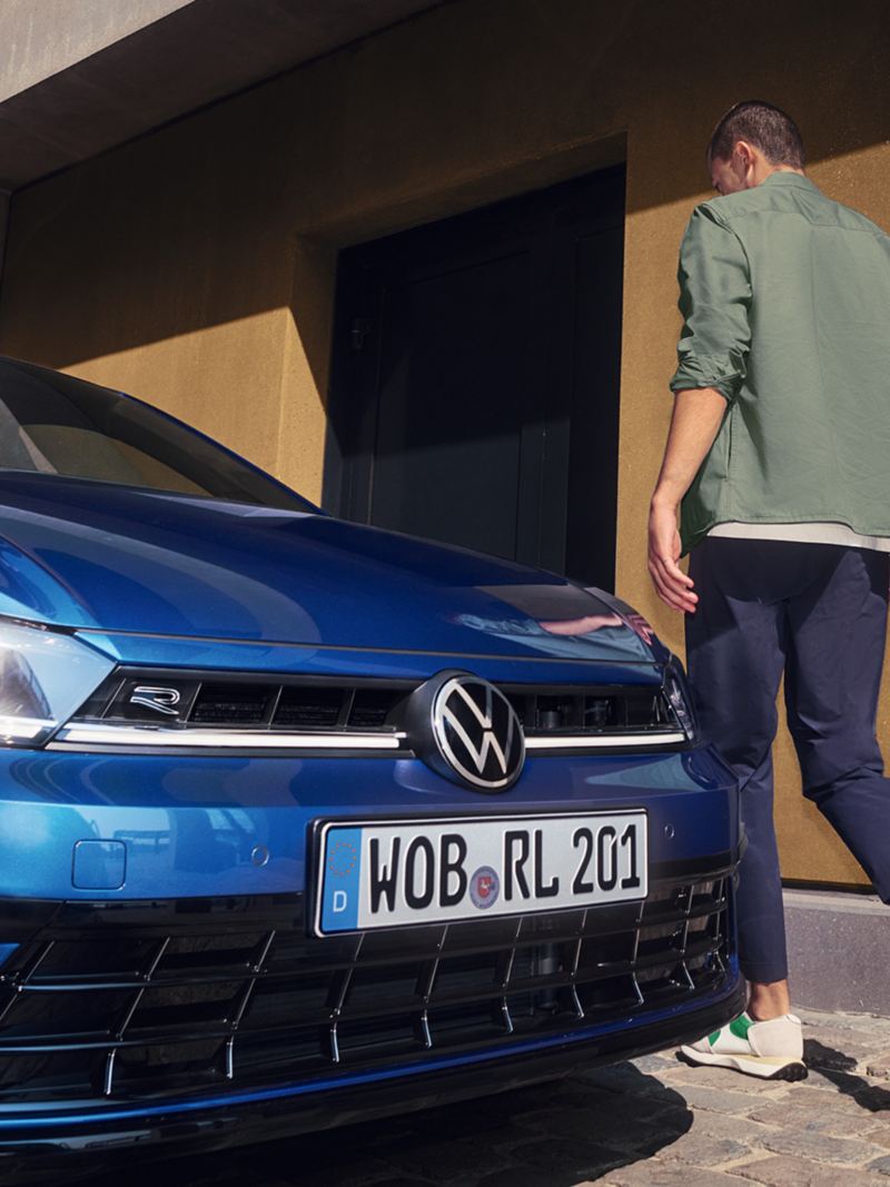 Λεπτομερής λήψη του μπροστινού μέρους ενός μπλε VW Polo με τους προβολείς IQ.LIGHT - LED matrix . Ένας άνδρας περνάει δίπλα του.