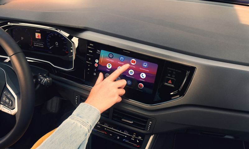 Système d'infodivertissement dans la VW Polo affichant Google Android Auto. Une main touche l’écran.