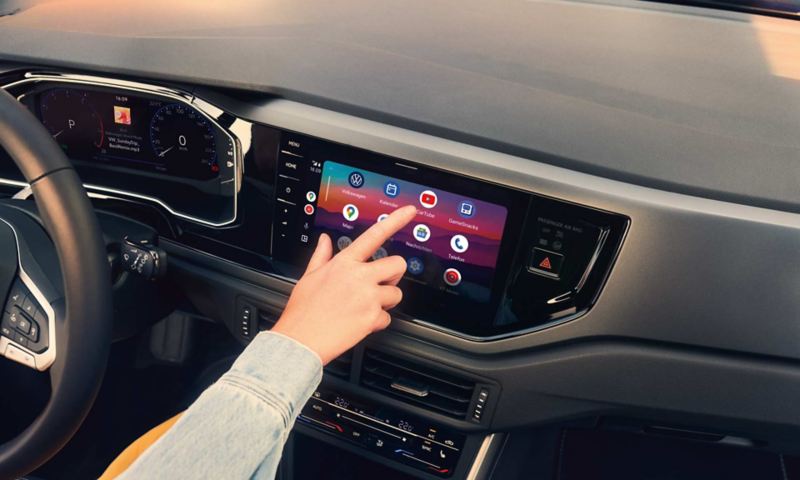 Display im VW Polo auf dem Android Auto™ von Google geöffnet ist. Eine Hand bedient das Display. 
